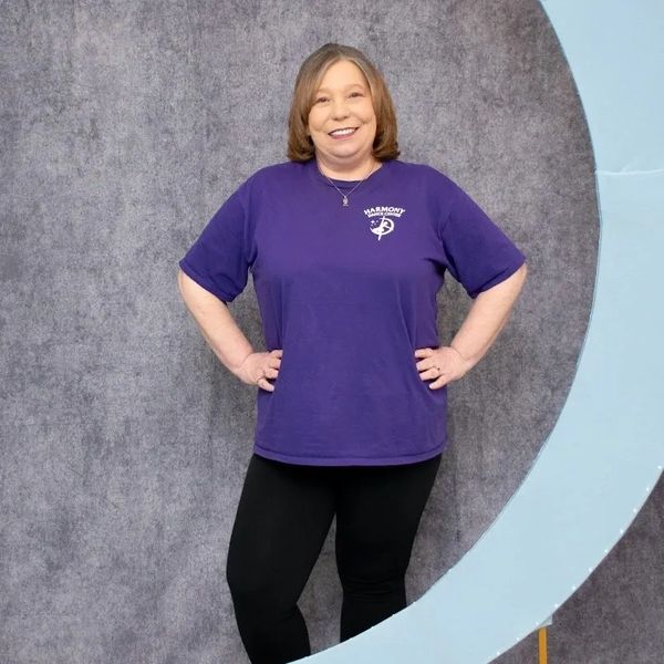 Woman smiling with hands on hips, wearing a purple shirt.