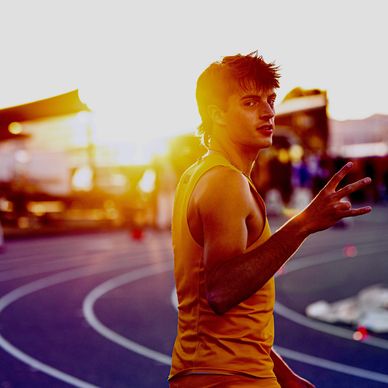 Athlete on track making a peace sign at sunset.