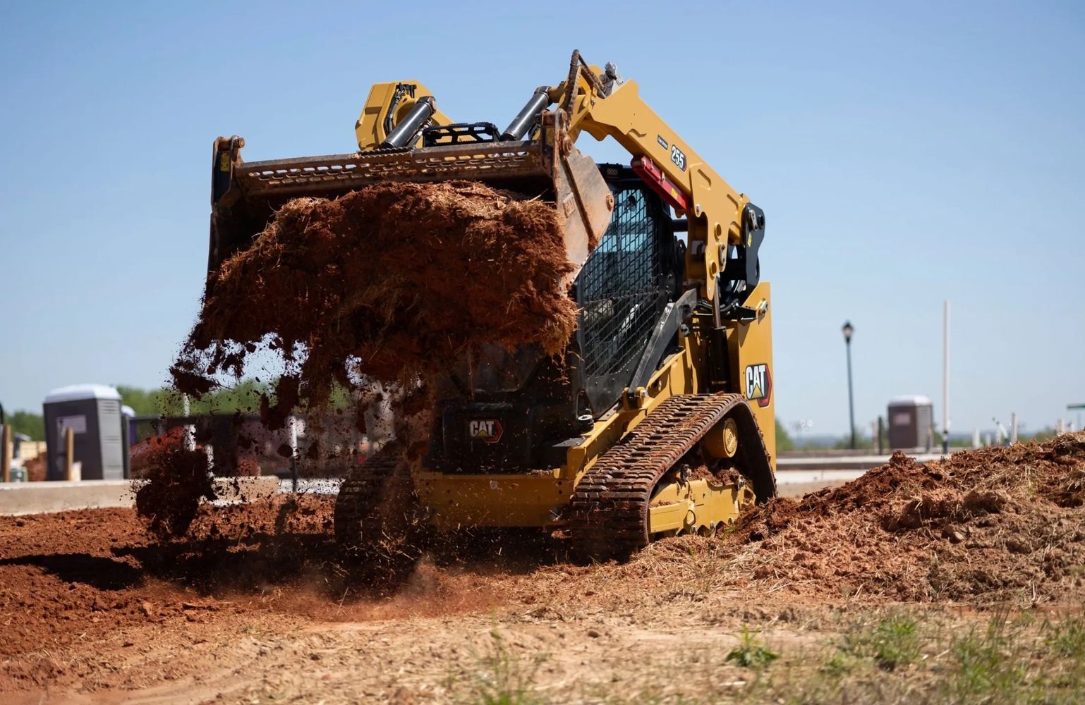 A yellow Caterpillar skid steer loader moving dirt at a construction site.