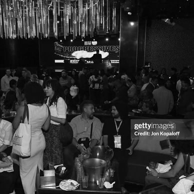 A lively crowd mingles at a music event with a DJ performing on stage under sparkling lights.