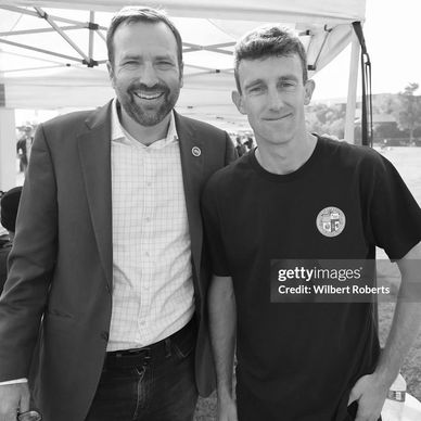 Two men smiling and posing under a tent outdoors.