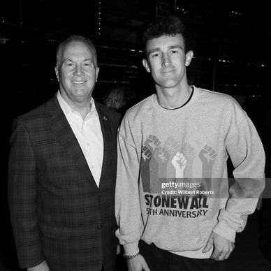 Two men posing together, one wearing a Stonewall 5th Anniversary sweatshirt.