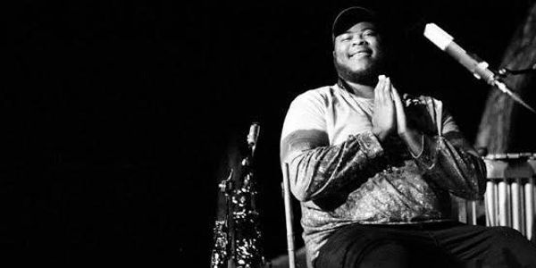 Man smiling with hands together near a microphone on stage.