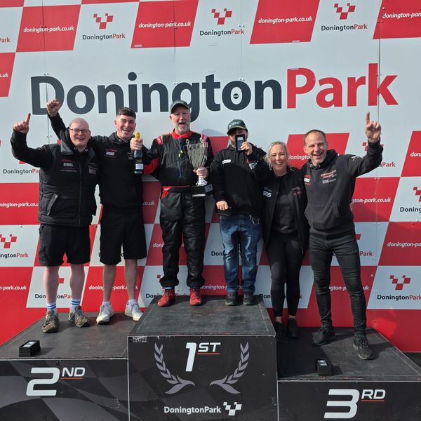 Happy racing team celebrates victory at Donington Park with trophies and champagne.