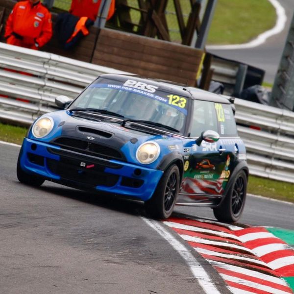 Blue Mini Cooper race car taking a sharp turn on a racetrack.