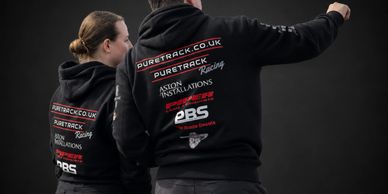 Two people in black hoodies with racing sponsor logos on the back, one pointing.