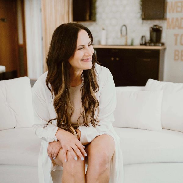 a women with dark long hair sitting on a white couch smiling
