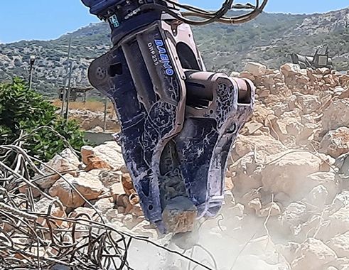 Heavy machinery crushing rocks amid rubble and dust.