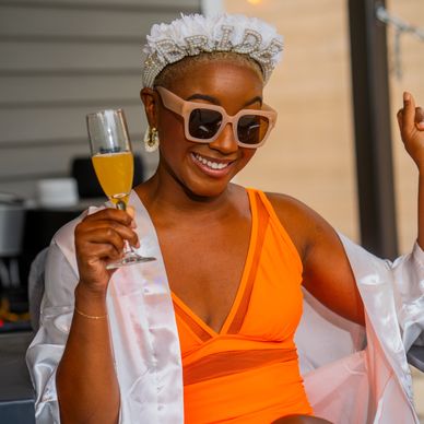 Woman celebrating, wearing a "BRIDE" headband and holding a glass of orange drink.