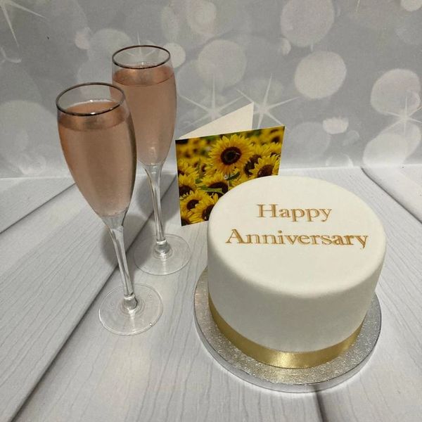 White anniversary cake with Happy anniversary message on a tab le with 2 glasses of prosecco