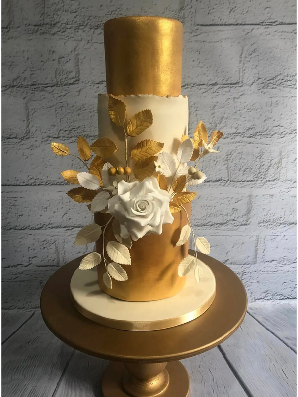 3 tier tall gold and ivory wedding cake with white rose, gold, ivory and white leaves on gold stand