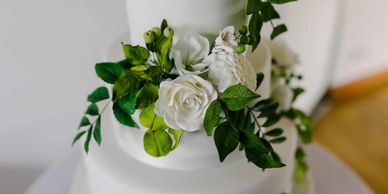 Handmade white sugar flowers on white cake including roses, pom pom dahlia, lisianthus, berries
