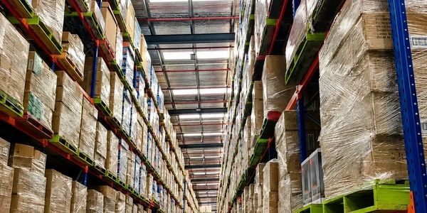 Warehouse aisle filled with tall stacks of palletized boxes wrapped in plastic.
