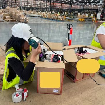 Warehouse worker inspecting items in boxes while using a tool.