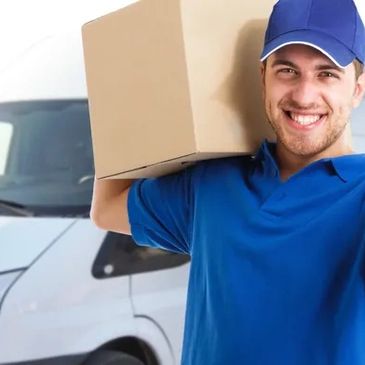 Smiling delivery man in blue uniform carrying a cardboard box near a van.