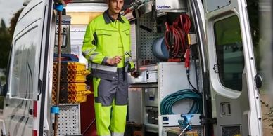 A worker in high-visibility clothing stands inside a well-organized utility van.