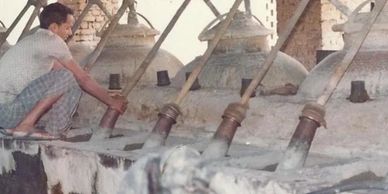 A man operates traditional distillation equipment with large vessels and pipes.