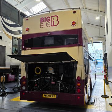 Double-decker bus with engine exposed in garage.