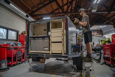 Man assembling a custom storage system in a trailer inside a workshop.