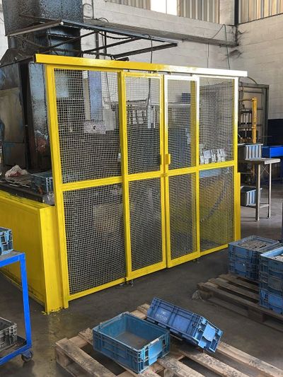 Yellow industrial safety cage with mesh doors in a factory setting.