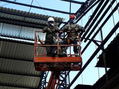 Two workers in safety gear on a suspended platform inside a building.