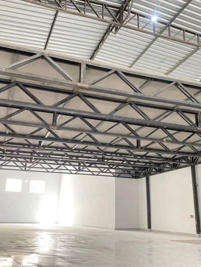 Spacious empty industrial warehouse with metal roof trusses and white walls.