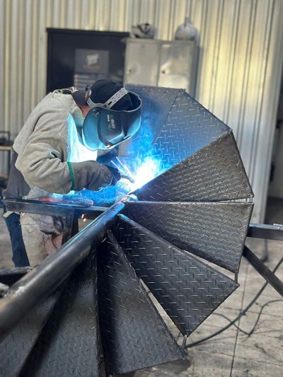A welder works on a metal spiral staircase with bright sparks.