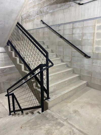 Concrete stairwell with black metal railing and handrails.