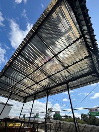A transparent roof structure under a bright blue sky with scattered clouds.