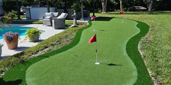 Backyard putting green with red flags near a pool and patio furniture.
