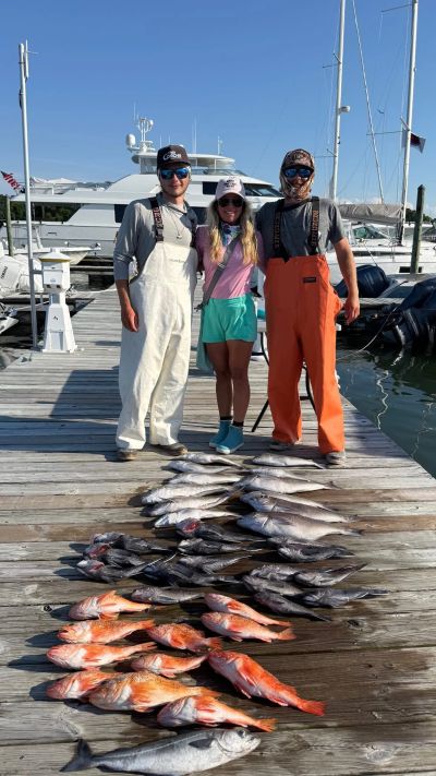 Three people standing by the dock with a large catch of fish laid out.