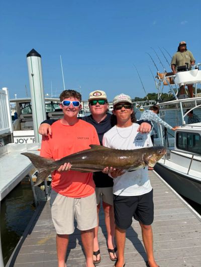 Three men on dock holding a large fish.