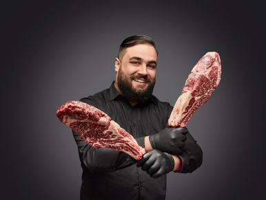Man holding two large raw steaks with a smile.