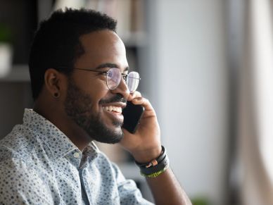 Smiling man talking on phone near window with natural light.