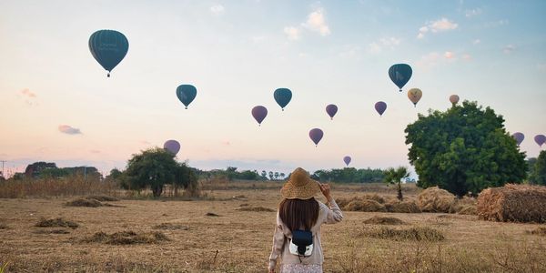 A person watches multiple hot air balloons in the sky during sunset.