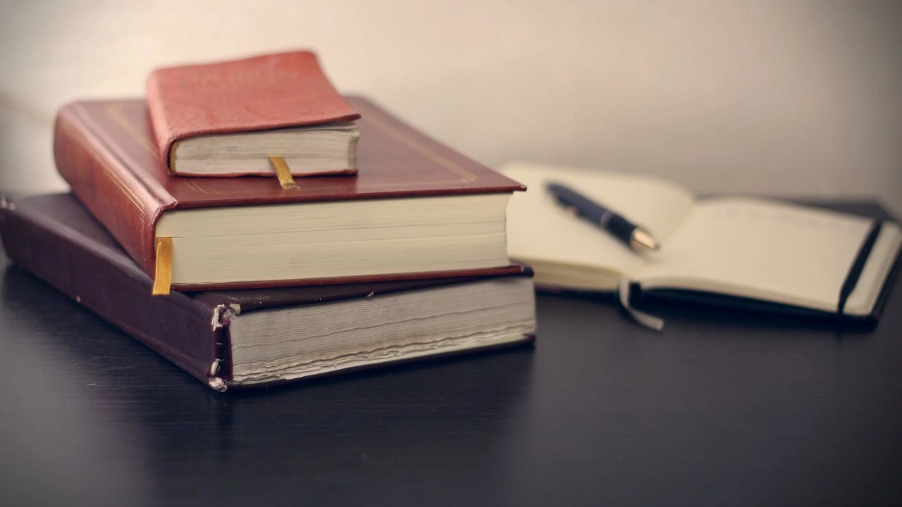 stack of books on a desk with open notebook and pen