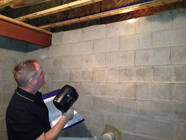 Dan Powell is checking a basement wall and ceiling for mold, mildew, and water leaks.