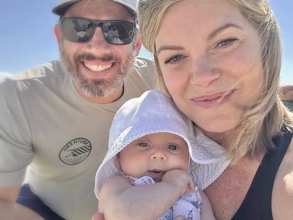 Smiling family selfie with baby in sun hat on a bright day.