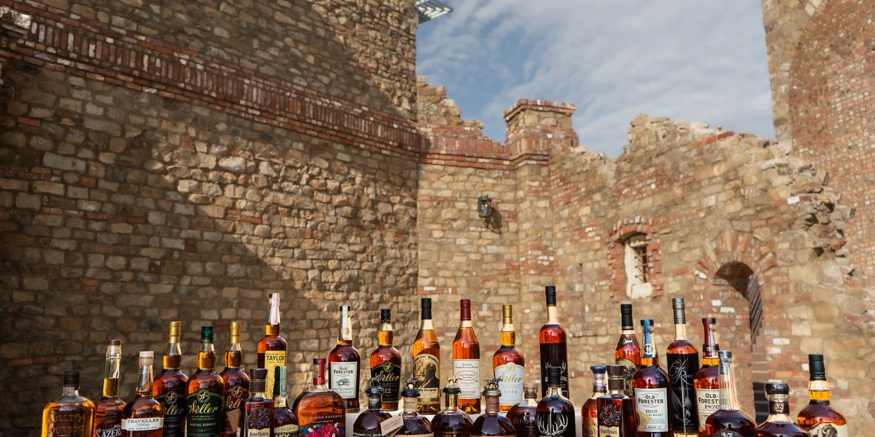 A diverse selection of bourbon whiskey bottles on display against a rustic stone wall.