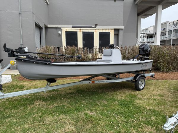 Gray fishing boat on a trailer outside a building.