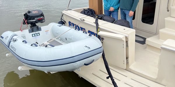 Small inflatable boat attached to the side of a larger boat on water.