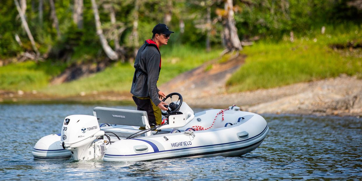 Man steering a small inflatable boat on calm water.