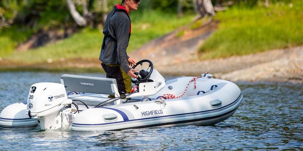 Man steering a white inflatable boat on calm water near shore.