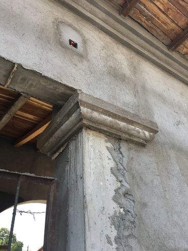 Close-up of a weathered concrete column with a crack and exposed brick above.