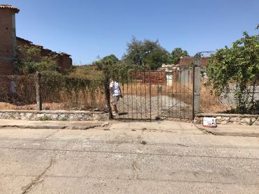 Man walking through a rusty metal gate on a dry, sunny day.