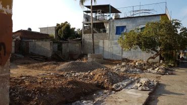 Construction site with a partially built structure and dirt piles under a clear sky.