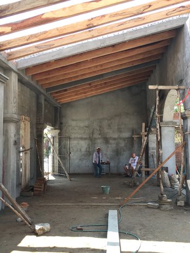 Construction site with workers under a wooden roof frame.