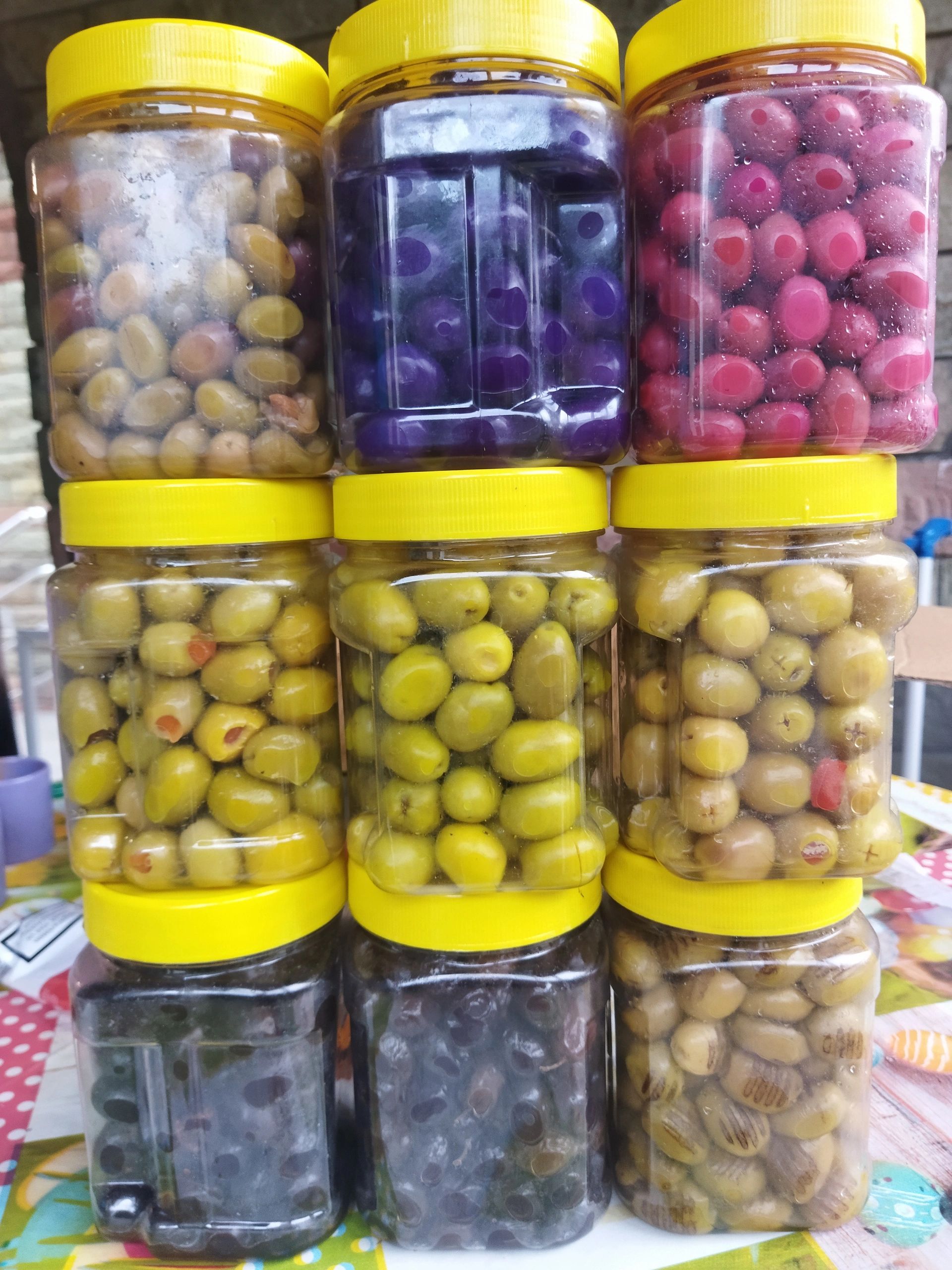 Stacked jars of various colorful pickled olives with yellow lids.