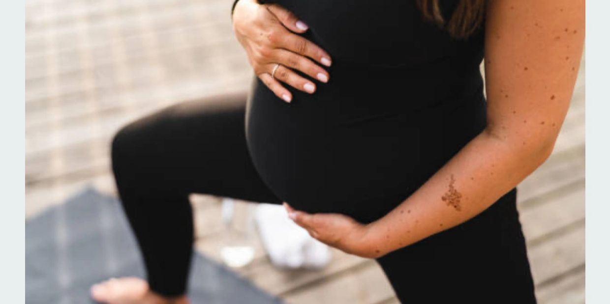 Pregnant woman holding her belly while doing a yoga pose.
