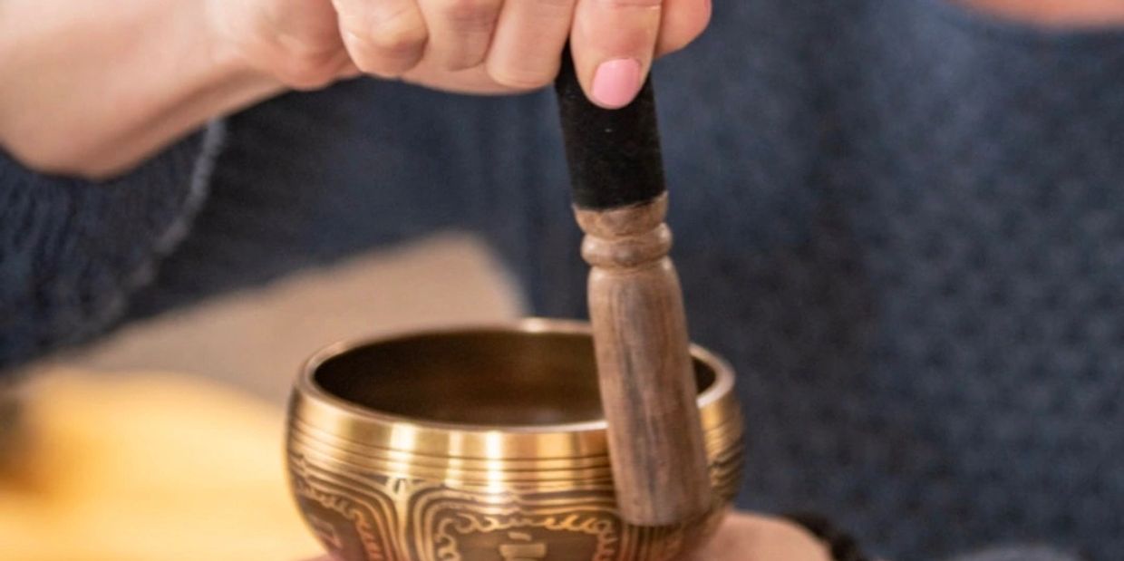 Person holding a wooden striker over a singing bowl.